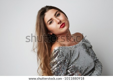 Close-up portrait of young beatiful woman wearing silver dress and posing at white empty studio background. Copy Space. Vertical. Front view