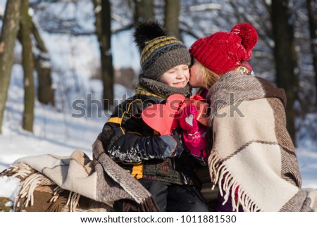 Romantic children valentines in winter forest. Little girl kissing boy with gift outdoors.