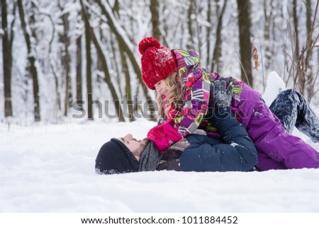 Man and little blondy girl in red hat playing in the snow white forest