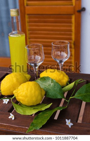 Lemonade or limoncello in a glass bottle, glasses, lemons with leaves on a serving table on the terrace