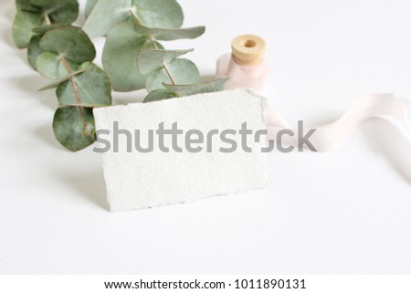 Bright feminine spring stationery mockup scene with a handmade paper greeting card, spool of silk ribbon and eucalyptus leaves on a white table background. Wedding styled stock photography.