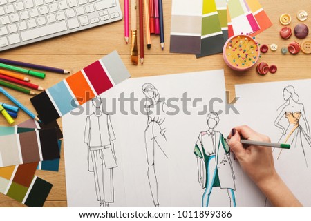 Top view on fashion designer at work. Female hands drawing clothes sketch at her creative workspace, top view