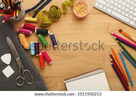 Fashion designer workspace top view. Sewing equipment, colored pencils, laptop and notepad on wooden table with copy space