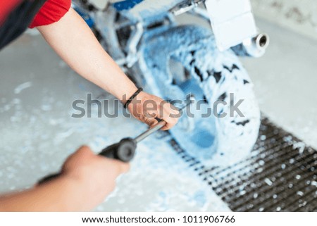 A man cleaning motorcycle with sponge using blue foam, car detailing (or valeting) concept. Selective focus. 