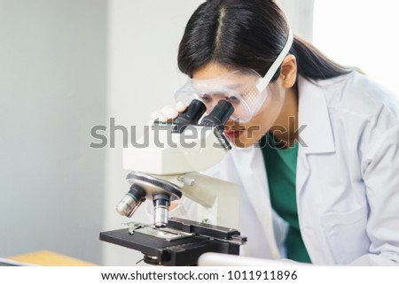 Female medical Doctor or research scientist looking through a microscope in a laboratory.science experiments,laboratory glassware containing chemical liquid for researching biology chemistry samples 