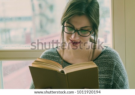 A girl in glasses reading a book near the window