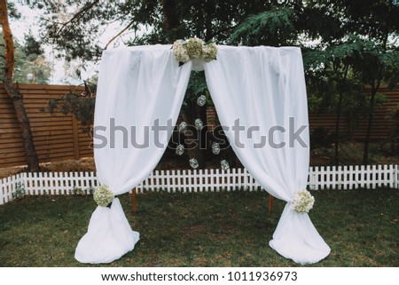 Wedding arch with white cloth and flowers in a minimalist style in the garden