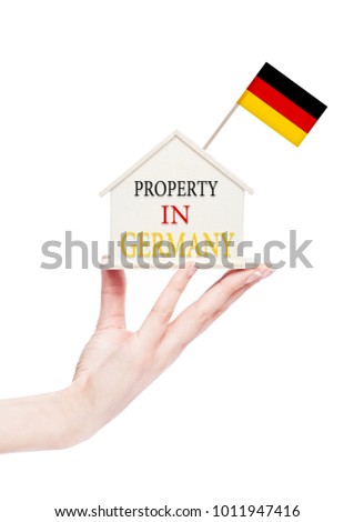 Female hand holding wooden house model with Germany flag on top. Property in Germany text