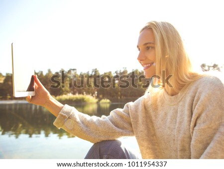 girl in an autumn park near a lake holds a tablet