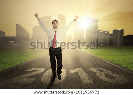 Picture of Italian male entrepreneur looks happy while running on the asphalt road with number 2018