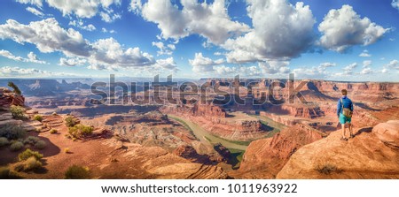 Panoramic view of young hiker standing on a cliff in in scenic Dead Horse Point State Park enjoying the view on a beautiful sunny day with blue sky and dramatic clouds in summer, Utah, USA Royalty-Free Stock Photo #1011963922