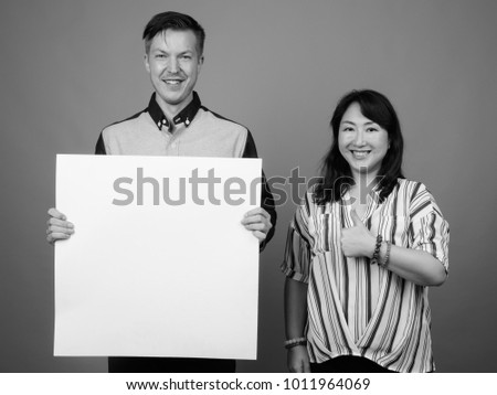 Studio shot of young handsome businessman and mature Asian businesswoman against gray background black and white