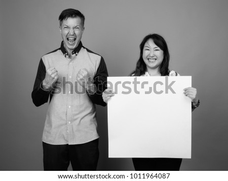 Studio shot of young handsome businessman and mature Asian businesswoman against gray background black and white