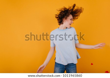 Spectacular short-haired girl in light-blue t-shirt dancing with pleasure. Indoor photo of pretty young female model with tattoo jumping on orange background.