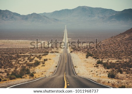 Classic panorama view of an endless straight road running through the barren scenery of the American Southwest with extreme heat haze on a beautiful sunny day with blue sky in summer Royalty-Free Stock Photo #1011968737