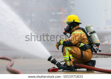 A fire fighter is controlling a fire monitor in order to combat fire. Visible water mist in the background.