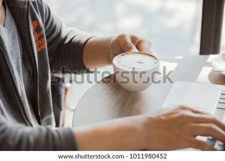 Close up of a hand of man holding a coffee cup beside a window in cafe.