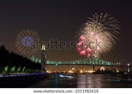 Montreal Clock Tower at night. Colorful fireworks explode over bridge, reflection in water. Montreal’s 375th anniversary. luminous colorful interactive Jacques Cartier Bridge. Old Port of Montreal.