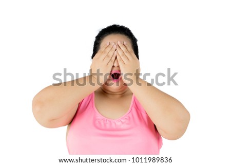 Picture of obese woman looks sad while closing her face with her hands, isolated on white background
