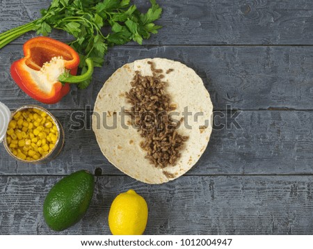 Cake made of cornmeal with ground beef on a wooden table and ingredients for Mexican tacos. A dish of Mexican cuisine.