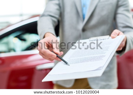Close up view  portrait of unrecognizable car salesman handing purchase contract to client buying brand new car in luxury showroom
