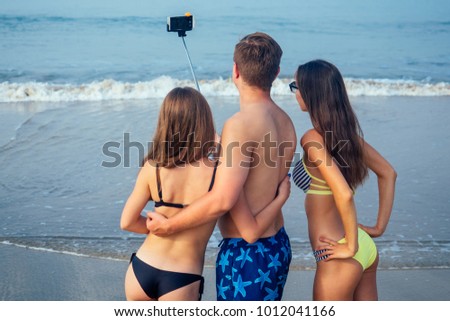 cheerful friends make a photo on the selfie-stick on the beach (view from the back)