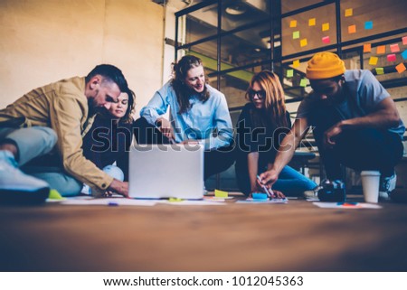 Group of designers making researchers during brainstorming session sitting on floor talking , team of creative co-workers using technology and papers planning startup collaborating on strategy