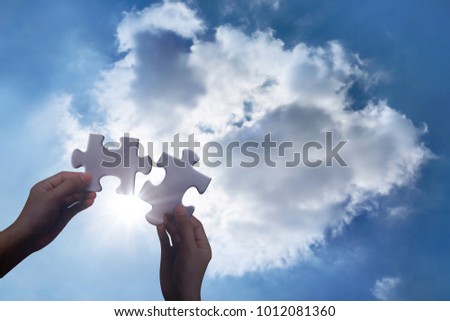 Two hands holding connecting two piece jigsaw heart puzzle at sky clouds background, teamwork concept.