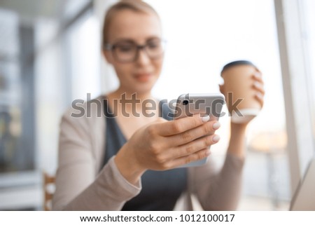 in focus is the phone in the hand of the woman with glasses, and in another glass of coffee