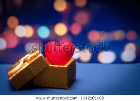 A red fabric heart in the golden present box with stripe on blur