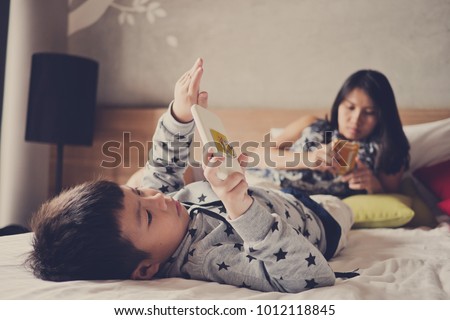 asian  chinese children playing tablet with mother on bed .  chinese child addicted phone. asian boy playing smartphone. kid use telephone. watching smartphone


