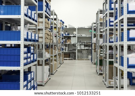 A small warehouse of spare parts and components of industrial electronics. Plastic trays and cardboard boxes in metal racks. Royalty-Free Stock Photo #1012133251
