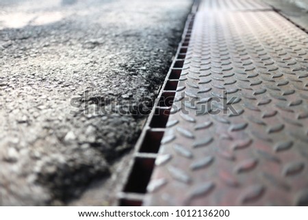 asphalt road or street with road side gutter with rusted dusted steel checkered plate cover left the side with small slots for water or rain water draining