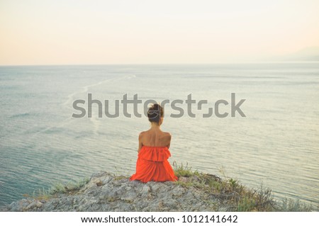 Outdoor lifestyle photo of woman in red dress looking at sea. Travel background. Tourism.