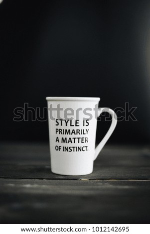 lettering of inspirational quote STYLE IS PRIMARILY A MATTER OF INSTINCT. on white mug, on the wooden black table and black background