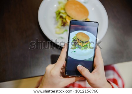 woman take picture of hamburger on her phone to share it after in socail networks