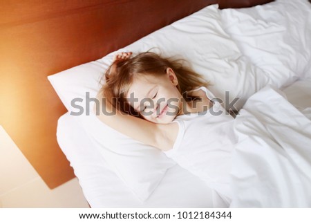 cute portrait of kid daughter sleeping and smiling laying at bed home on sunny good morning. concept of kids sleep, care or childhood