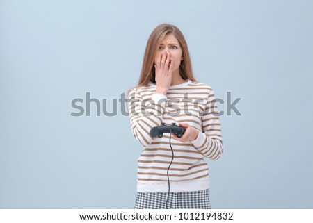 Upset woman with video game controller on color background