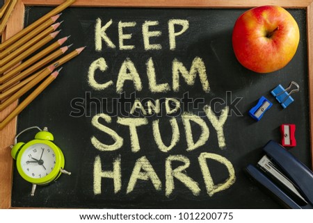 Composition with phrase "Keep calm and study hard" and stationery on chalkboard, top view