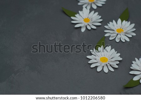 White chamomiles made of artificial material. The flowers are on a neutral green background.