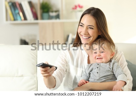 Happy mother and baby watching tv sitting on a couch in the living room at home