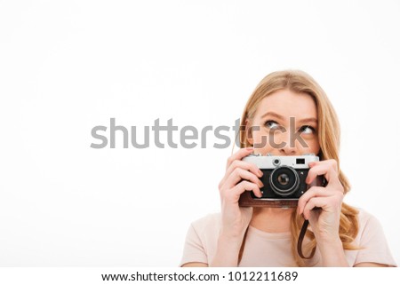 Photo of cute young woman standing isolated over white background. Looking aside holding camera.
