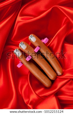 3 sausages with false nails placed in a manicure spacer like fingers on a vibrant red satin background. Minimal funny and quirky pop still life photography