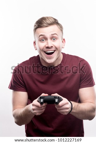 Showing nice results. Upbeat fair-haired young man holding a video game controller and smiling brightly, being excited to play a game