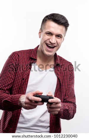 Enjoying himself. Cheerful young man holding a controller and playing a video game while being excited about it and smiling widely