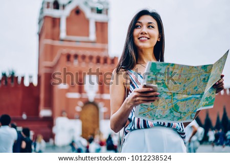 Attractive asian female traveler standing on red square in Moscow enjoying sightseeing tour with map,cheerful woman tourist getting to location near Kremlin on background planning next route in Moscow Royalty-Free Stock Photo #1012238524