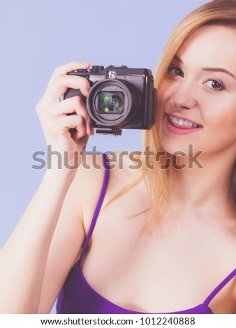 Photographer girl shooting images. Lovely blonde smiling woman with camera on violet blue background