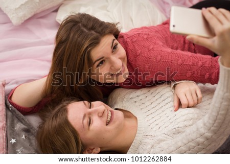 Two girls doing selfie for social networks lying on the bed