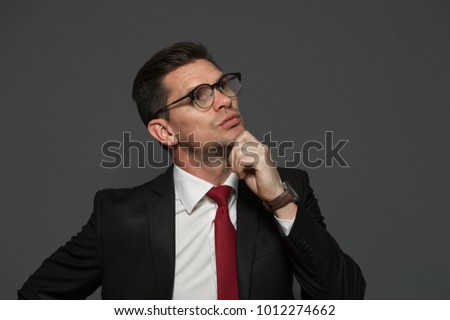 Thoughtful businessman with glasses and formal attire ponders about shares and growing exchange rate looking somewhere far away on a gray background. Copyspace