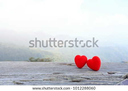 A red heart with two hearts rests on an old wooden floor with a green backdrop and a blank space for texting on Valentine's Day.